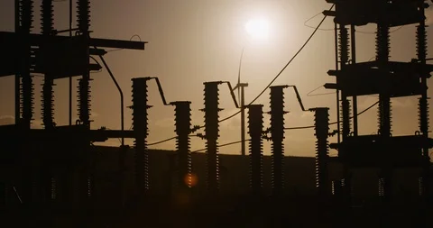 Power plant with wind tower in background silhouetted against the sun. Stock Footage 86887688
