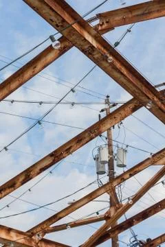 Power pole and transformers set against a blue sky, seen thru rusted girders Stock Photos