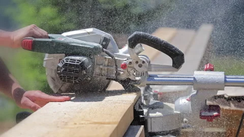 Power saw cuts a thick timber board while sawdust sprays through the air Stock Footage 346605075