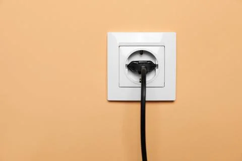 Power socket with inserted plug on pale orange wall. Electrical supply Stock Photos