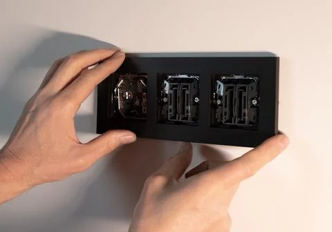 Power socket outlet frame plate installation on white wall. Hands placing b.. 库存照片