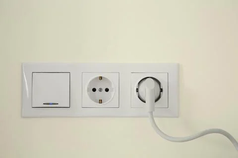 Power sockets with inserted plug and light switch on white wall indoors Stock Photos