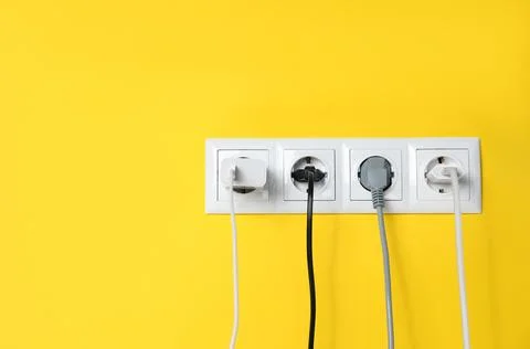 Power sockets with inserted plugs on yellow wall, space for text. Electrica.. Foto stock