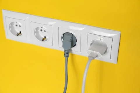 Power sockets with inserted plugs on yellow wall, closeup. Electrical supply Stock Photos