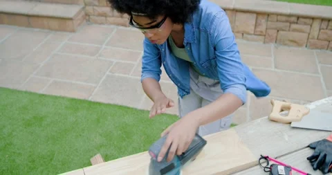 Power switch being pressed, orbital sander is smoothing wood plank on backyard Stock Footage 335748214