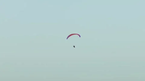 Powered paraglider canopy arcing across clean sky while paramotor pilot cruising Stock Footage 334323624