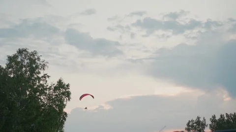 Powered paraglider flying over grass field at dusk under pastel sky Stock Footage 317179319