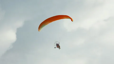 Powered paraglider paramotor trike with vibrant orange green wing flying high 스톡 동영상 318201423