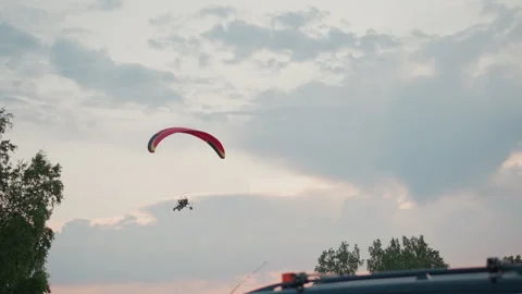 Powered paraglider with red canopy soaring above trees during golden hour Stock Footage 317200312