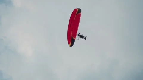 Powered paraglider soaring overhead under cloudy sky with red canopy Stock Footage 317155914