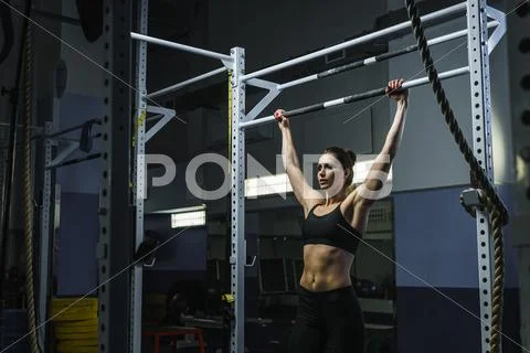 Powerful attractive woman CrossFit trainer do pull ups during workout Stock Photos