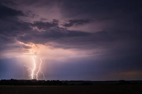 Powerful cloud-to-ground lightning strike over rural landscape at night Foto stock