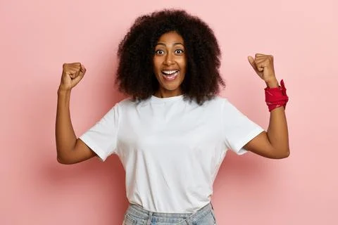 Powerful dark skinned curly haired woman shows muscles with arms raised Stock-Fotos