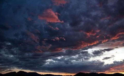 Powerful dramatic storm clouds illuminated by vibrant pink sunset light. Stock Photos