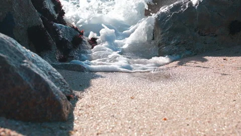 Powerful foamy white ocean wave gushing through gap between rocks on beach Stock Footage 146054983