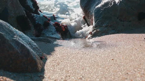 Powerful foamy white ocean wave splashing through gap between rocks on beach Видео 146055072