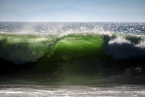 Powerful green ocean wave cresting with sunlight and distant mountains Fotos de archivo