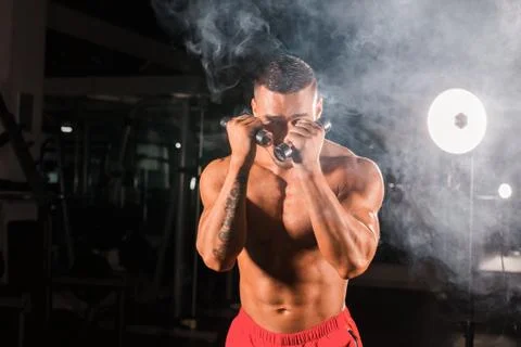 Powerful man doing boxing exercises, making direct hit with dumbbells. Photo of Stock Photos