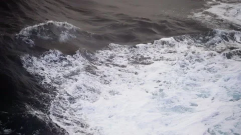 Powerful ocean waves collide and churn into frothy white foam across dark Stock Footage 316776669