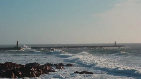 Powerful ocean waves crash against a large concrete pier with two lighthouses Stock Footage 323606477