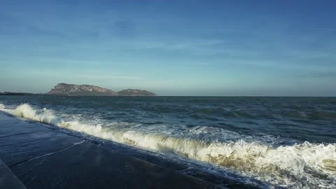 Powerful ocean waves crash against dark concrete shore with distant islands Stock Footage 326243301