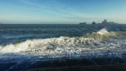 Powerful ocean waves crash against dark concrete shore with distant islands Stock Footage 331042242