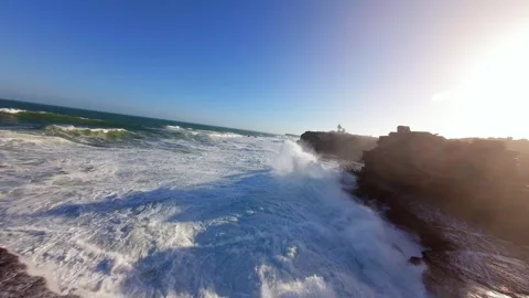 Powerful ocean waves crash against dark rocks under clear blue sky at Peniche 스톡 동영상 346076791