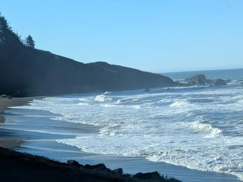 Powerful ocean waves crash onto sandy shoreline within a rocky cove Stock Photos