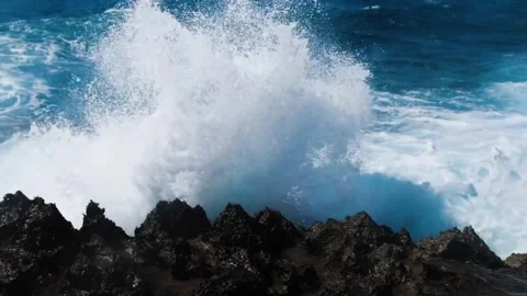 Powerful ocean waves crashing against sharp volcanic rocks on a sunny day Vidéo 334353258