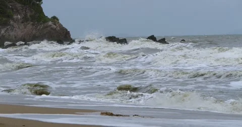 Powerful ocean waves crashing against rugged rocks along shore beneath cloudy Stock Footage 345281849
