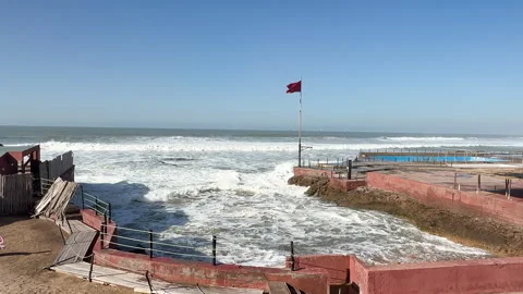 Powerful ocean waves hitting a coastal with Morocco flag waving Video stock 332739299