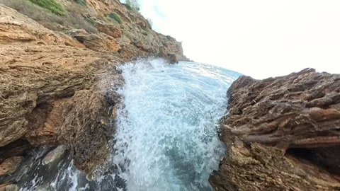 A powerful slow-motion shot of a wave crashing forcefully into rugged coastal Stock Footage 293740737
