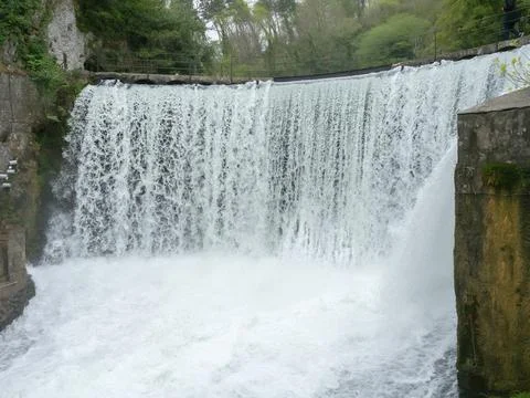 Powerful splashing stream of a waterfall. The waterfall flows down from the dam Stock Photos