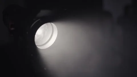 A powerful spotlight emits a focused beam of light, cutting through gentle mi Stock Footage 326003550