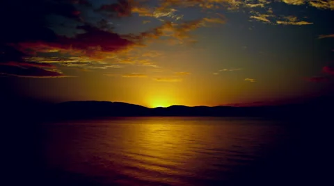Powerful sunrise timelapse with blue and gold sky and red clouds over water Stock Footage