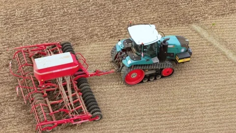 Powerful tracked tractor with red seeding implement on harvested farmland. Wide Stock Footage 346604913
