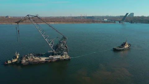 Powerful tugboat pulling large floating crane by river against background of Stock Footage 188088226