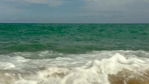 Powerful turquoise ocean waves crash onto the sandy shore beneath dramatic Video stock 337929106