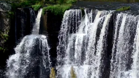 A powerful waterfall cascades over rocks in a lush, green landscape Stock Footage 312679857