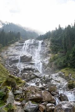 Powerful waterfall cascading down a rocky mountain face in a lush forest. Stock Photos