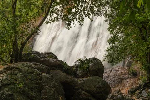 A powerful waterfall cascading down a steep, rocky cliff surrounded by lush, Stock Photos