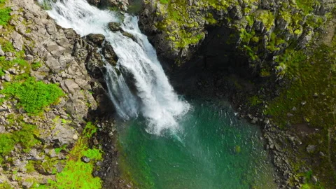 Powerful waterfall cascading over fractured basalt cliff into emerald lake Stock Footage 344822166