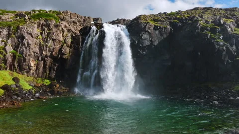 Powerful waterfall cascading over fractured basalt cliff into emerald lake Stock Footage 344822257