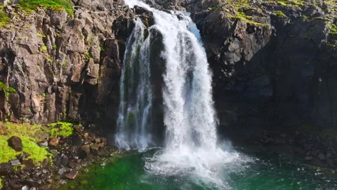 Powerful waterfall cascading over fractured basalt cliff into emerald lake Stock Footage 344822522