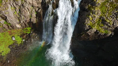 Powerful waterfall cascading over fractured basalt cliff into emerald lake Stock Footage 344822650
