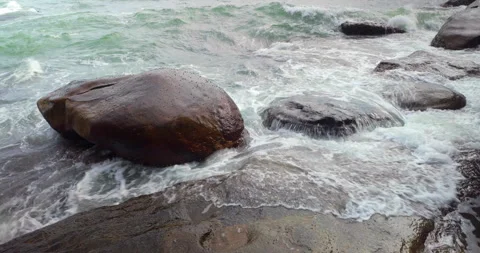 Powerful wave explodes in a white splash against a massive, dark boulder. Stock Footage 312537914