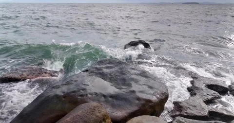 Powerful wave explodes in white spray against a massive, dark boulder. Stock Footage 313093659