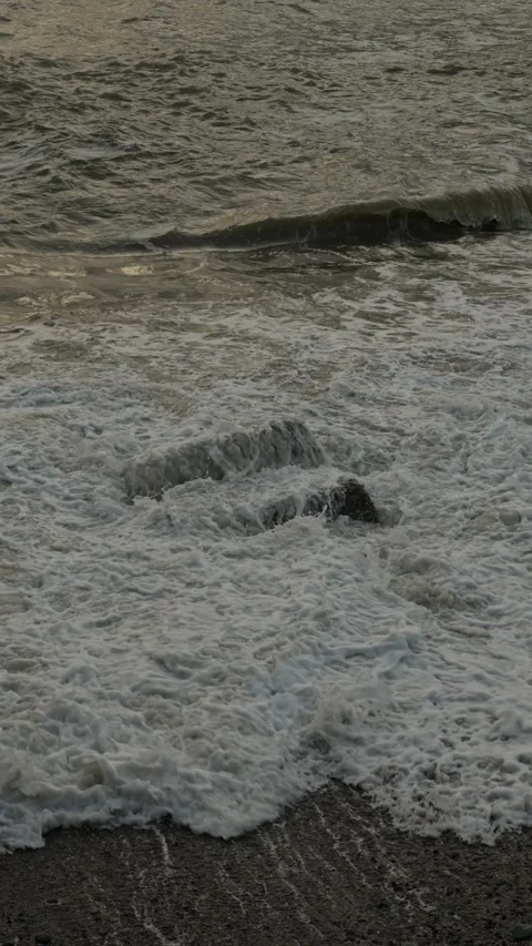 Powerful waves break against jagged stones during sunset glow 動画素材 335950601