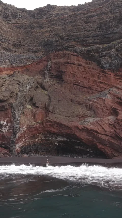 Powerful waves breaking against black volcanic sand in a vertical video, red 스톡 동영상 308395844
