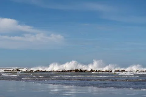 Powerful waves crash against rugged rocks under a clear sky Stock Photos